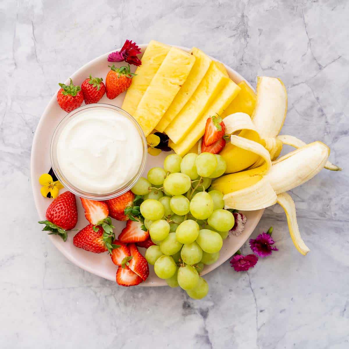 A plate full of fresh strawberries, grapes, bananas and pineapple and the Whipped cottage cheese dip in a glass ramekin