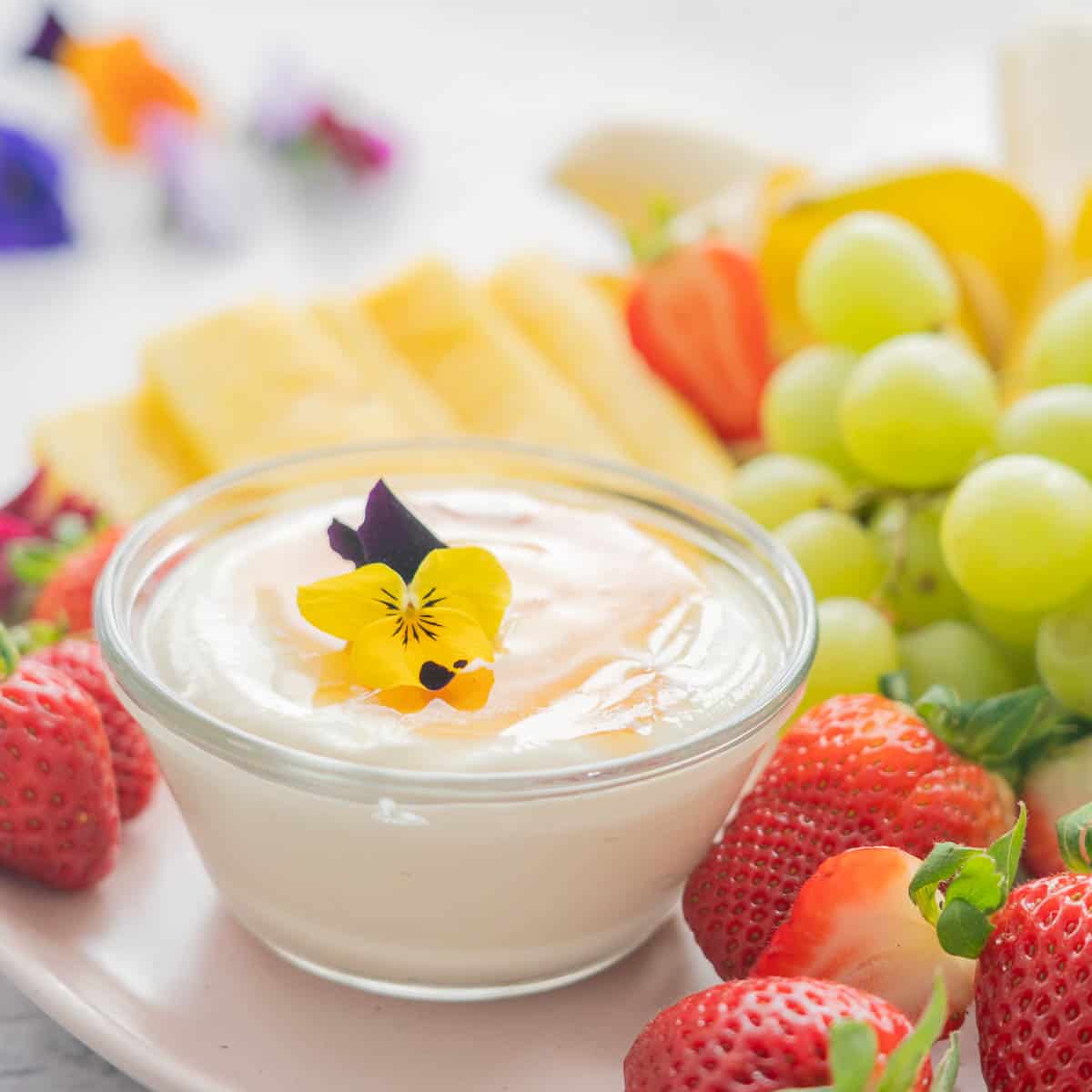 A plate full of fresh strawberries, grapes, bananas and pineapple and the Whipped cottage cheese dip in a glass ramekin