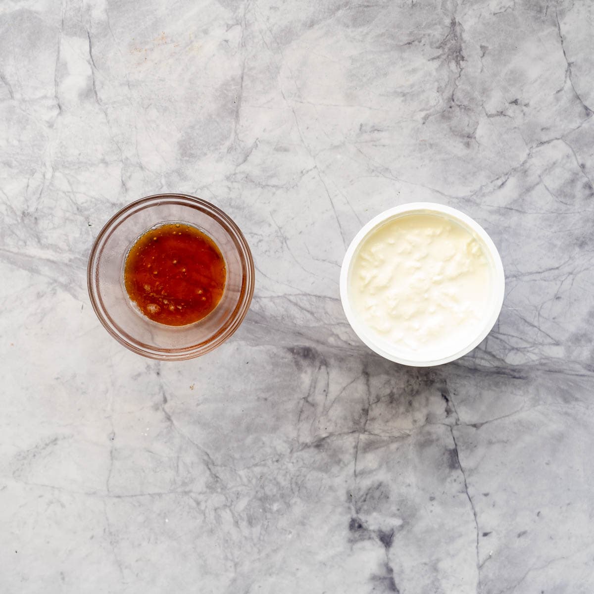 A small ramekin of honey sitting next to a tub of cottage cheese laid out on the bench
