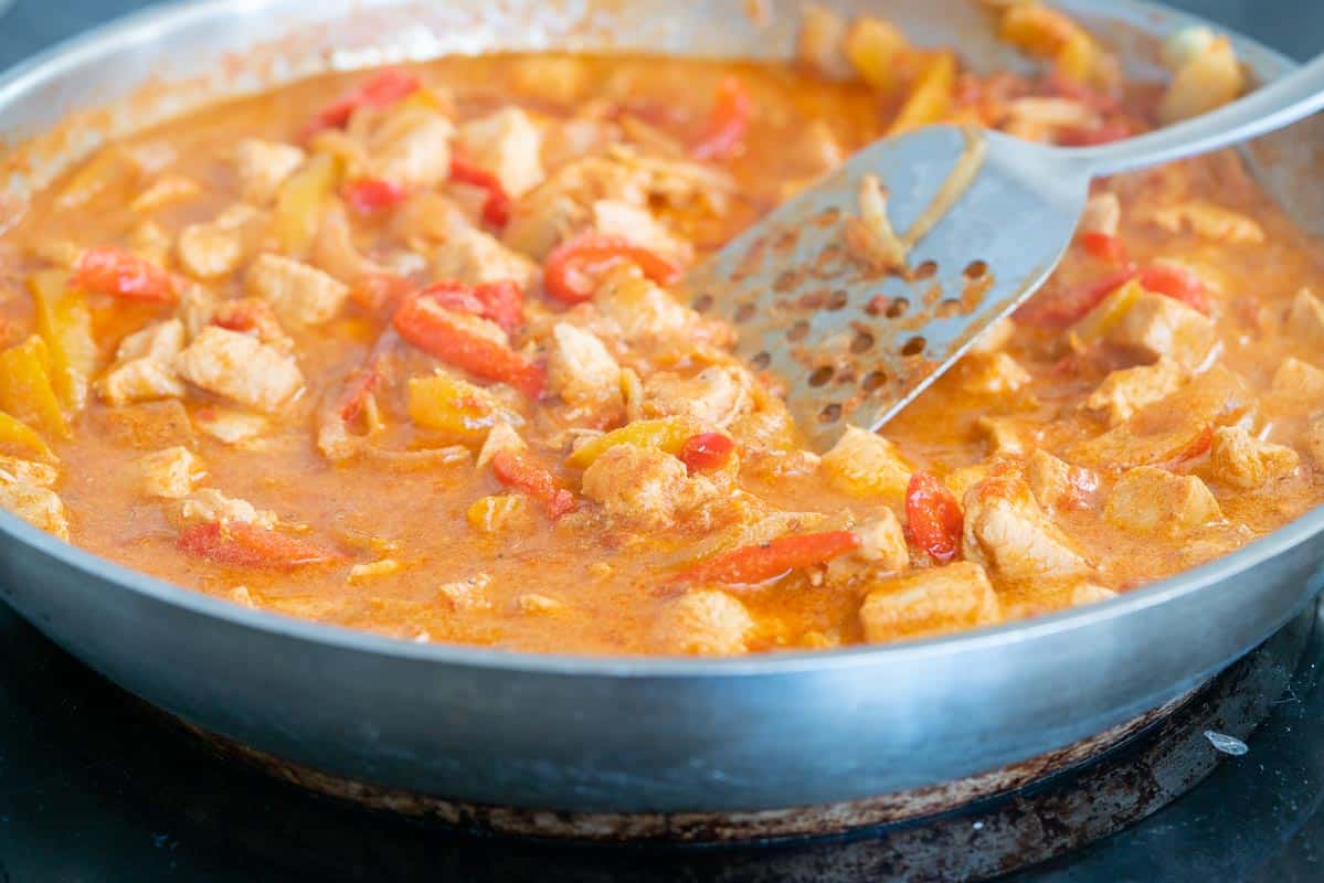 A frying pan of simmering chicken paprikash with a spatula resting on the side