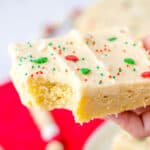 Hand holding a cookie bar with bite taken out of it, decorated with green and red sprinkles for Christmas.