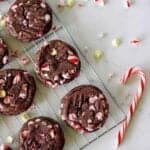 Double chocolate peppermint cookies on a cooling rack decorated with Christmas colours and candy cane on bench top.