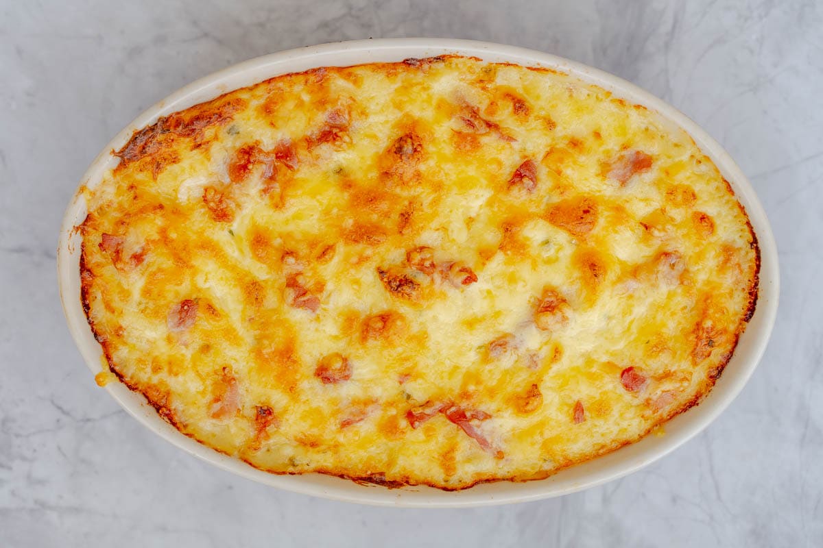 Golden baked mashed potatos in a serving dish sitting on the bench.