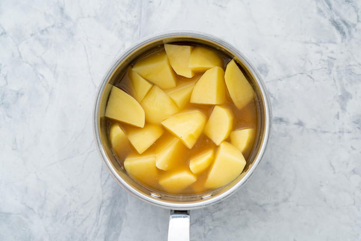 A pot of peeled and cut up potatoes in chicken broth sitting on the bench