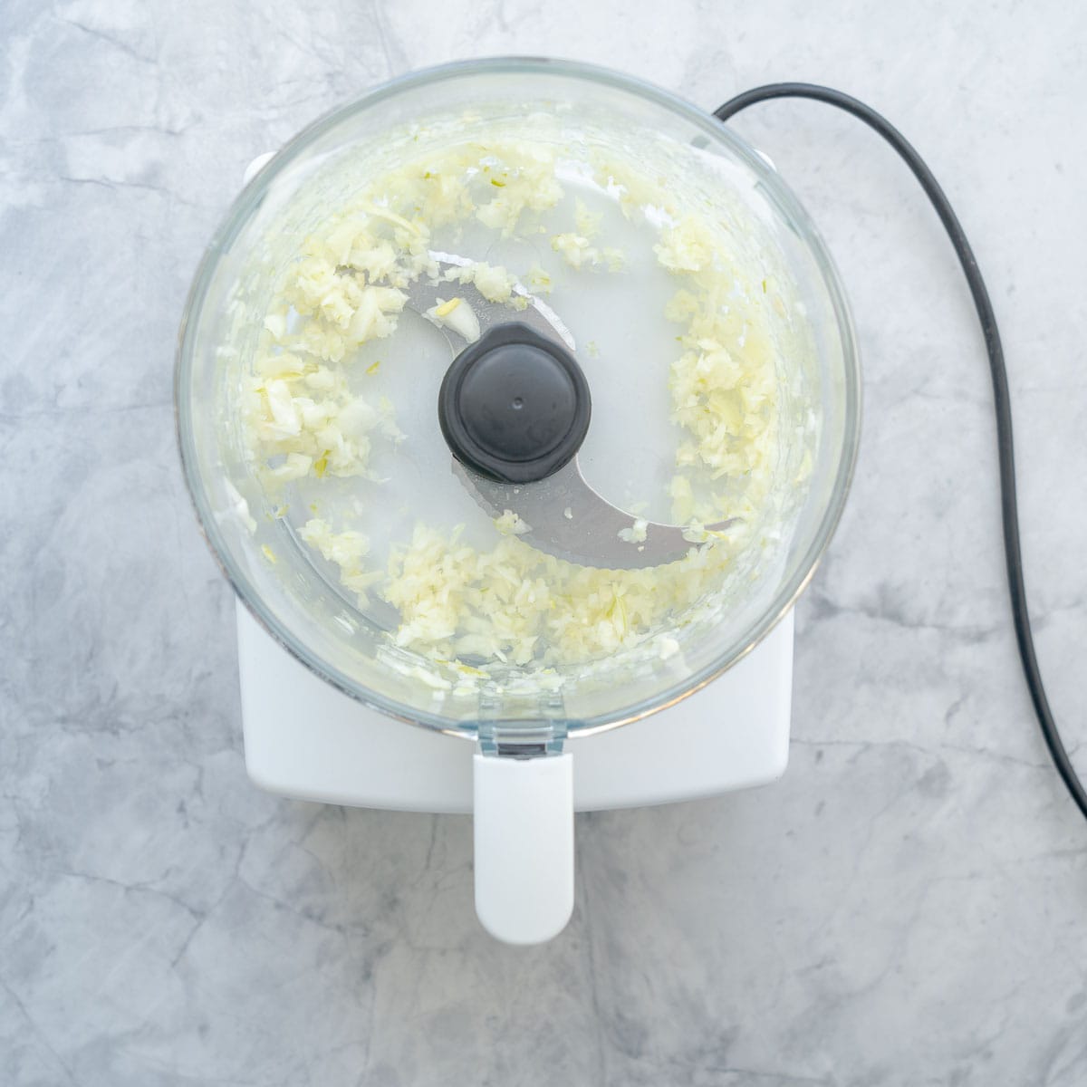 A food processor sitting the bench with the lid off and finely diced onions.