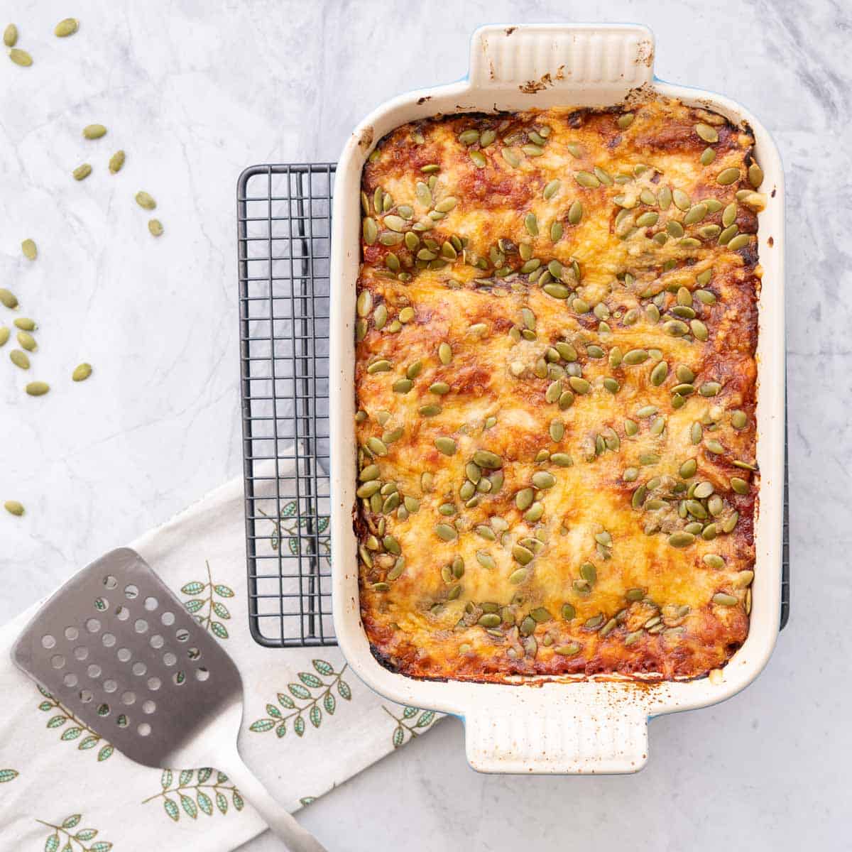 A baking dish of golden brown baked Butternut Squash Pasta cooling on a baking rack on the bench with a sprinkling of pepitas