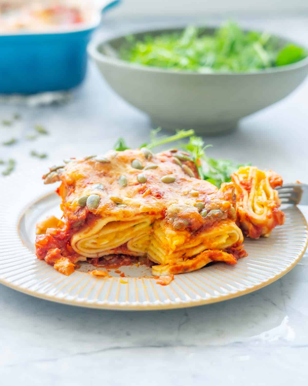 A serving of Butternut Squash Pasta on a plate with a serving bowl of salad in the background.