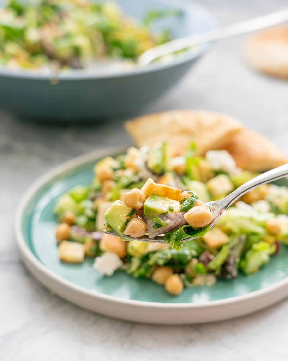 A forkful of salad with chickpeas, avocado, feta and green vegetables on a fork.