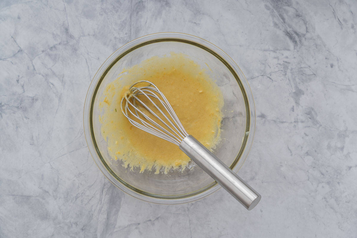 A large glass mixing bowl with a creamy mustard salad dressing whisked in the bottom of it.