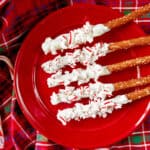 Pretzel sticks on a red plate half covered in white chocolate and red sprinkles.