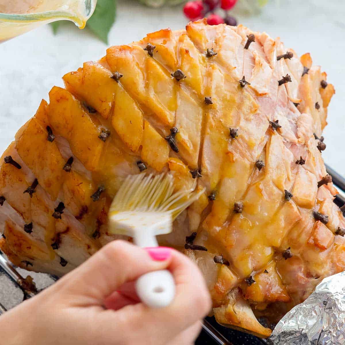 A hand brushing glaze into the fat layer of the cooked ham