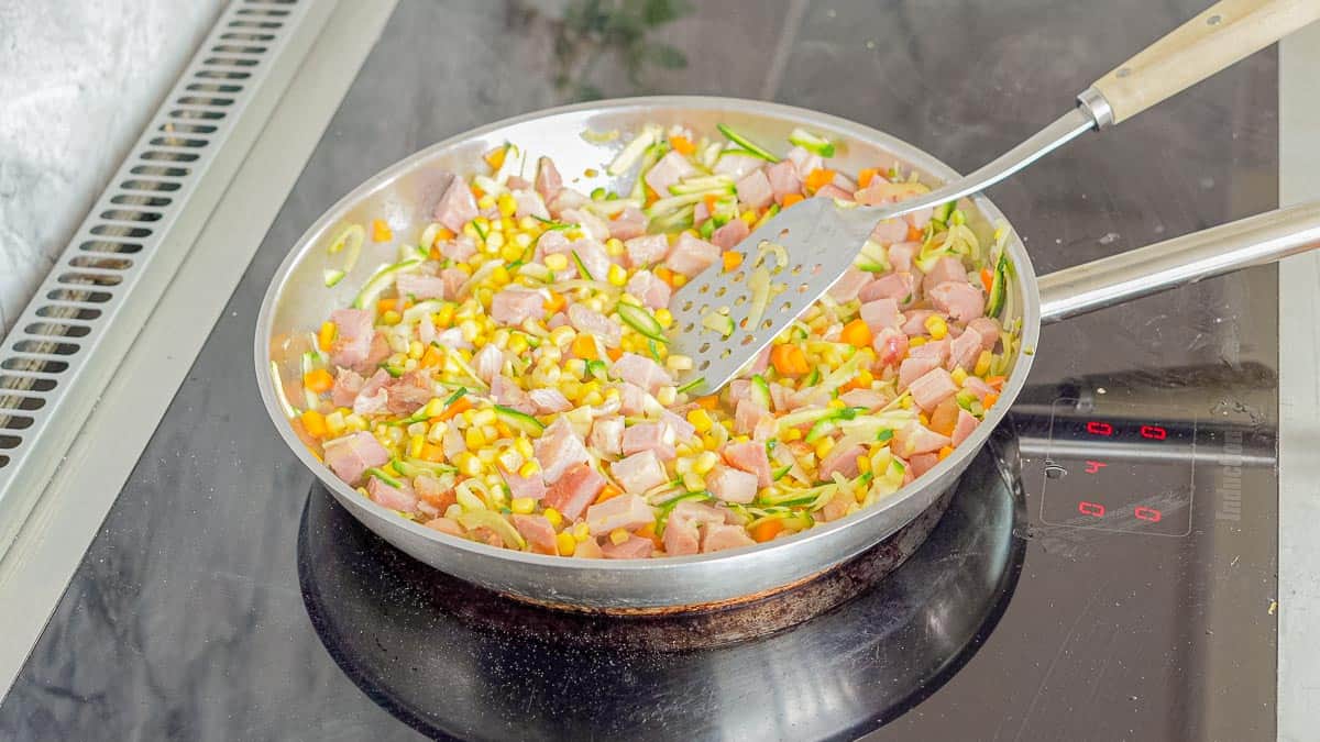 Sautéing onions, zucchini, carrots, corn kernals and ham in a frying pan on a induction element.