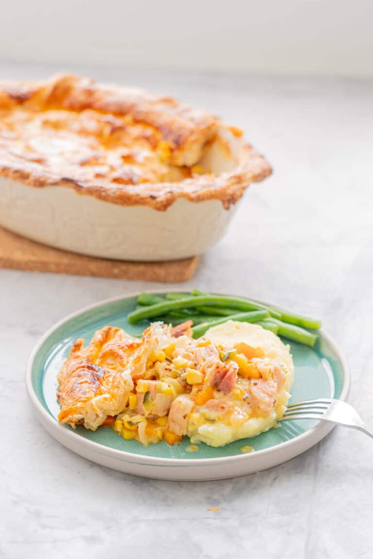 a serving of Ham Pot Pie with a side of blanched beans on a teal coloured ceramic plate and with a fork resting on the side, sitting the bench