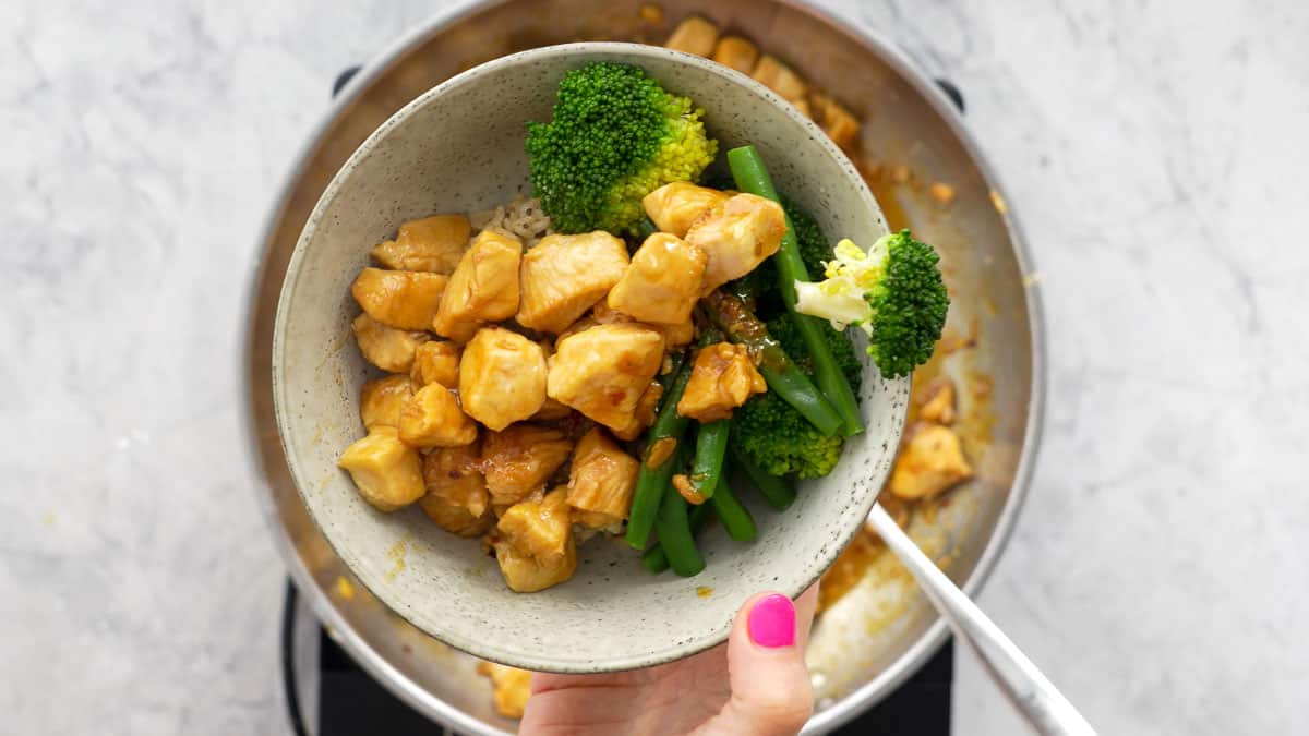 A small serving of honey garlic chicken with a side of blanched beans and broccoli held above the rest of the dish below