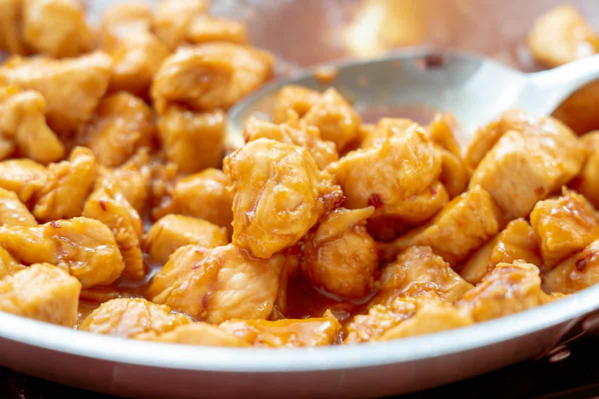 Honey garlic chicken pieces in a pan with a serving spoon resting on the side