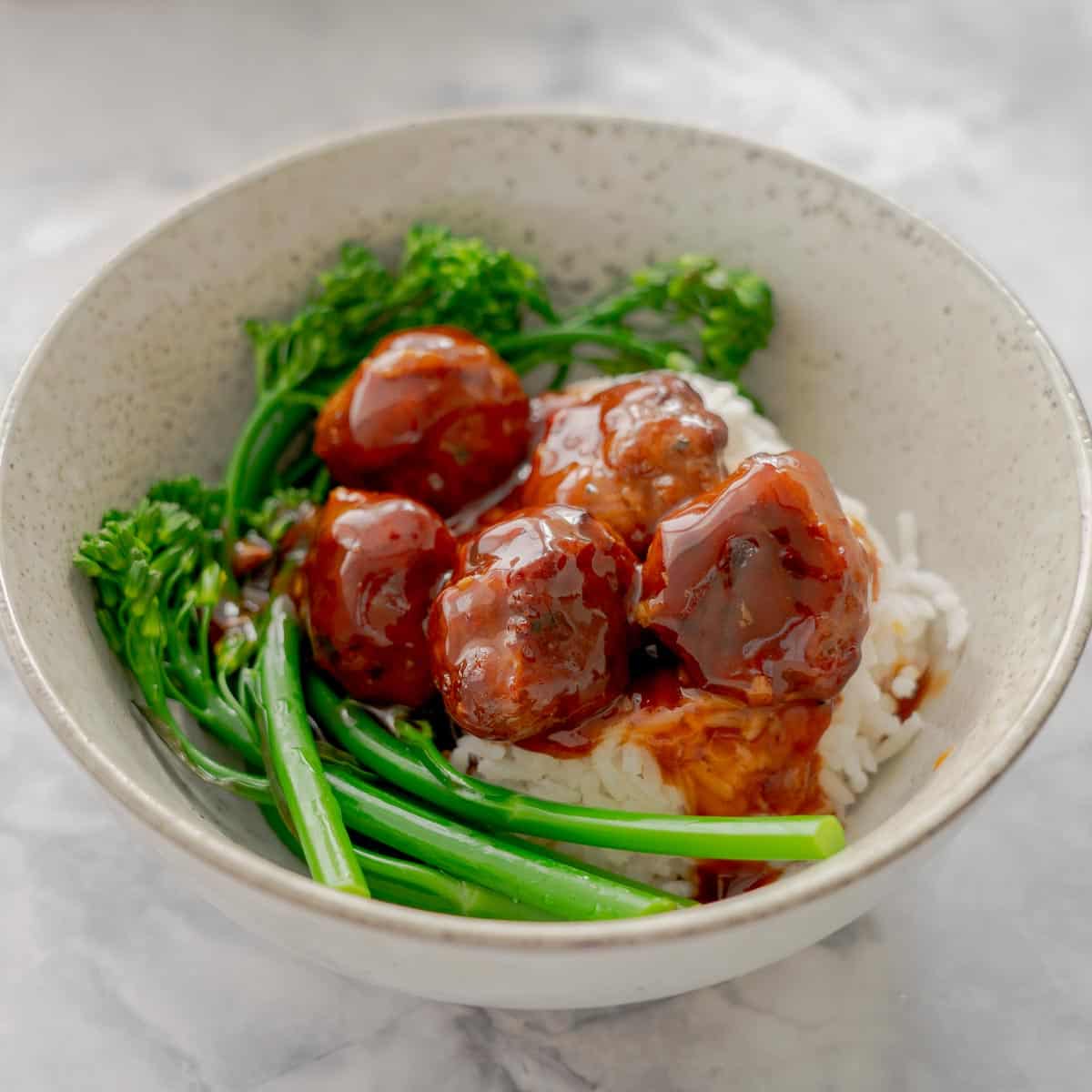 Sticky glossy honey meatballs served on a bed of rice with broccolini on the side.