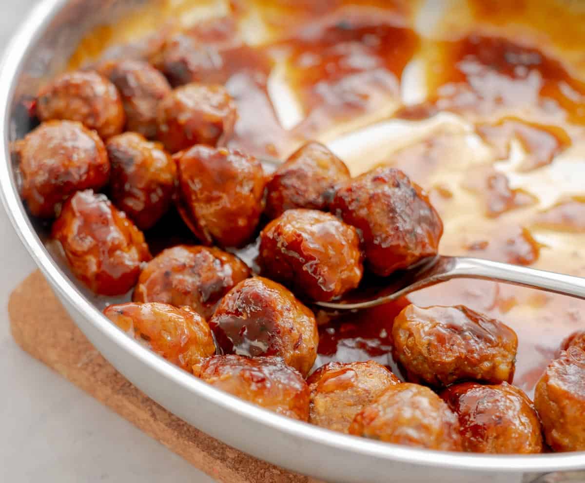 Sticky, glossy Honey Garlic meatballs being scooped out of frypan.