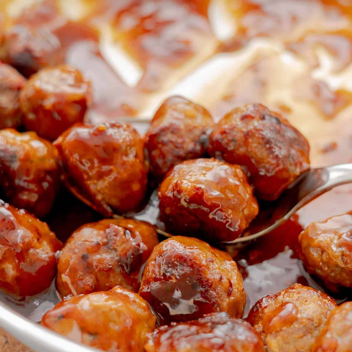 Sticky, glossy Honey Garlic meatballs being scooped out of frypan.