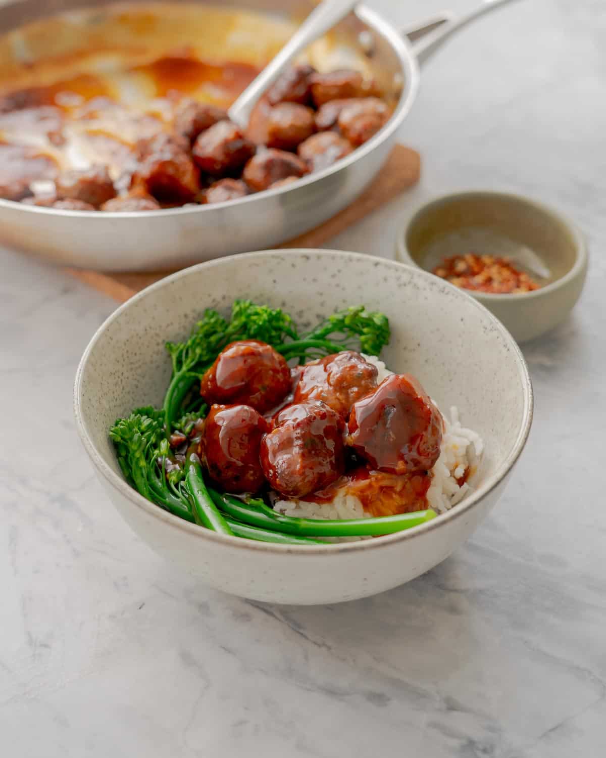 A bowl with meatballs in a sticky sauce, steamed brococlini and rice.
