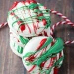 Four cookies stacked on benchtop covered with white icing and drizzled red and green icing on top.