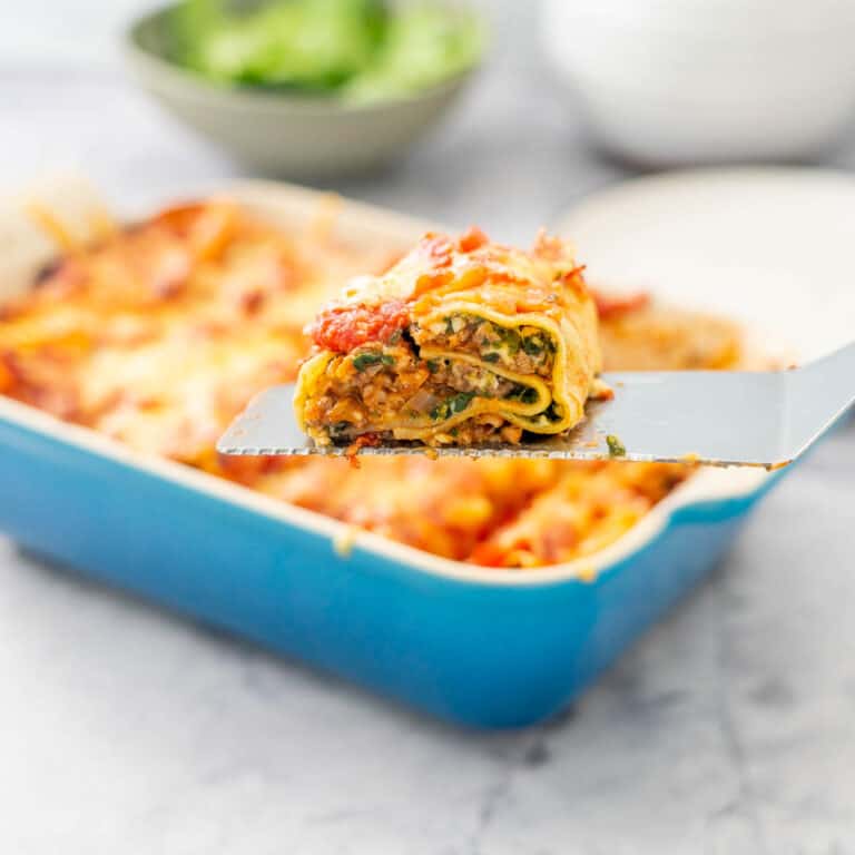 A lasagna roll being held on a spatula above a casserole dish of lasagna roll ups.
