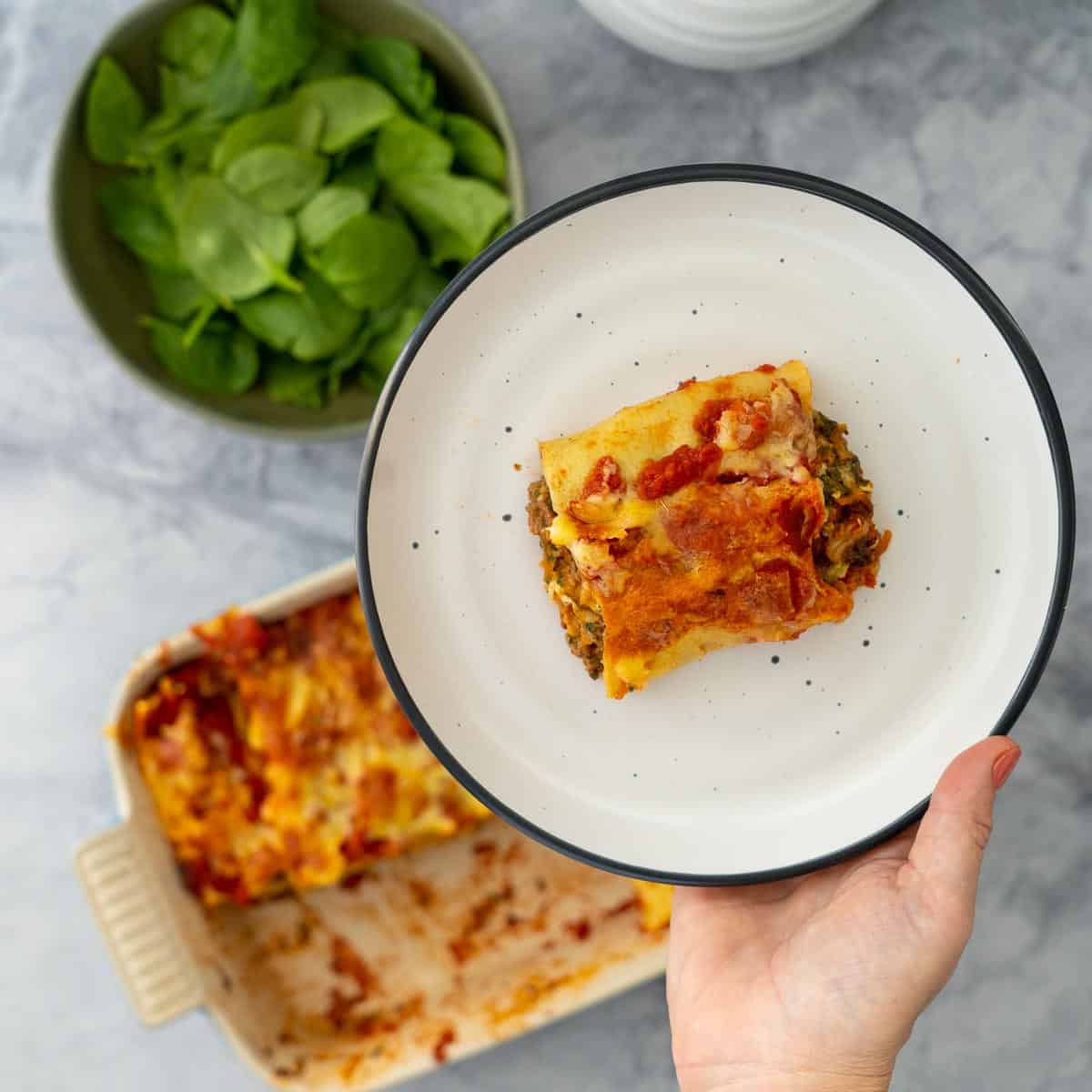 A slice of baked Lasagne roll up served on a plate that someone is holding.