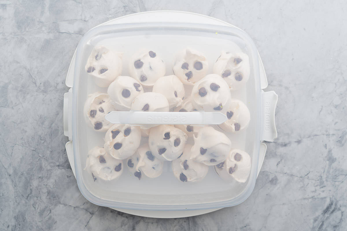 A plastic cake carrier full of meringue cookies sitting on the bench.