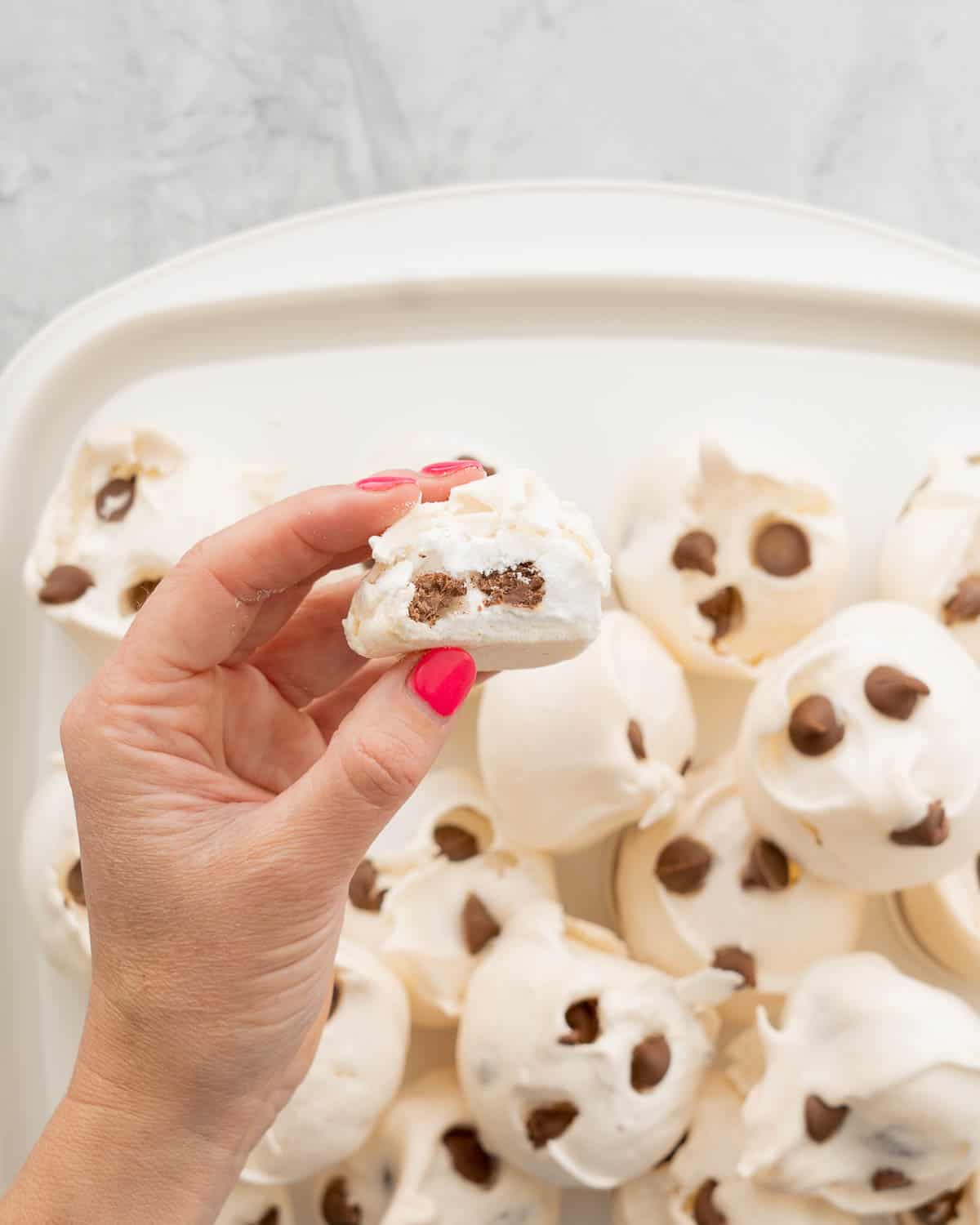 A hand holding a halved meringue cookie above the rest of the batch below.
