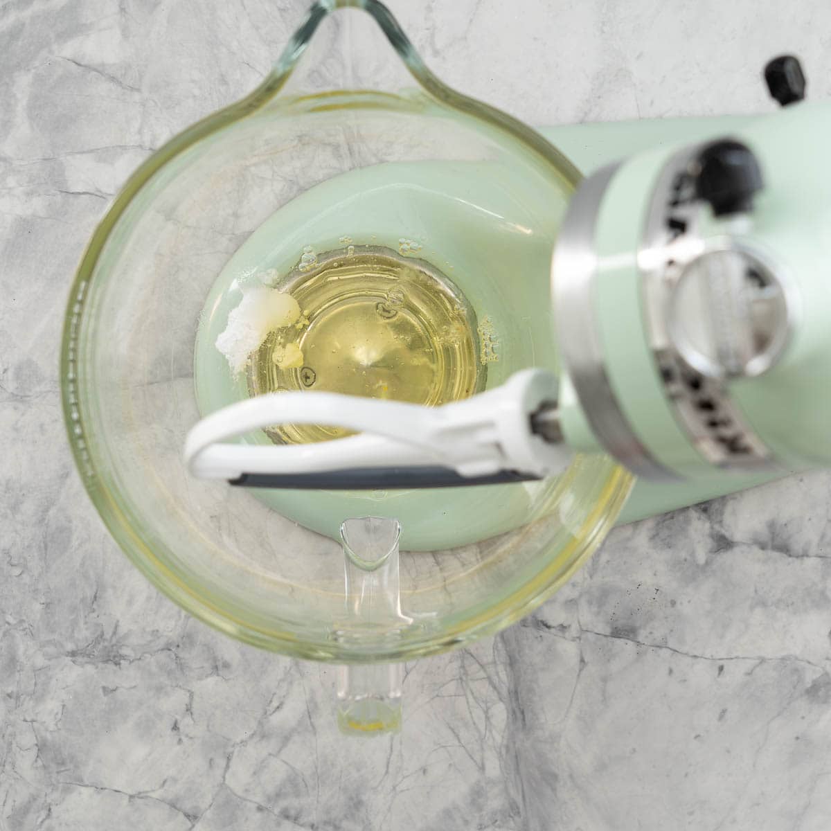 A stand up mixer with egg whites, cream of tartar and salt sitting on the bench.