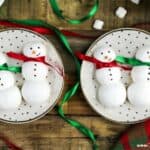 Two plates with two snowman meringues on each plate, red and green ribbon around their necks as scarfs.