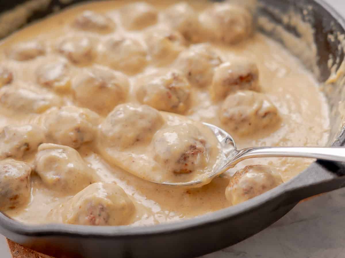 A batch of sweedish meatballs in a cast-iron pan with a spoon resting on the side.