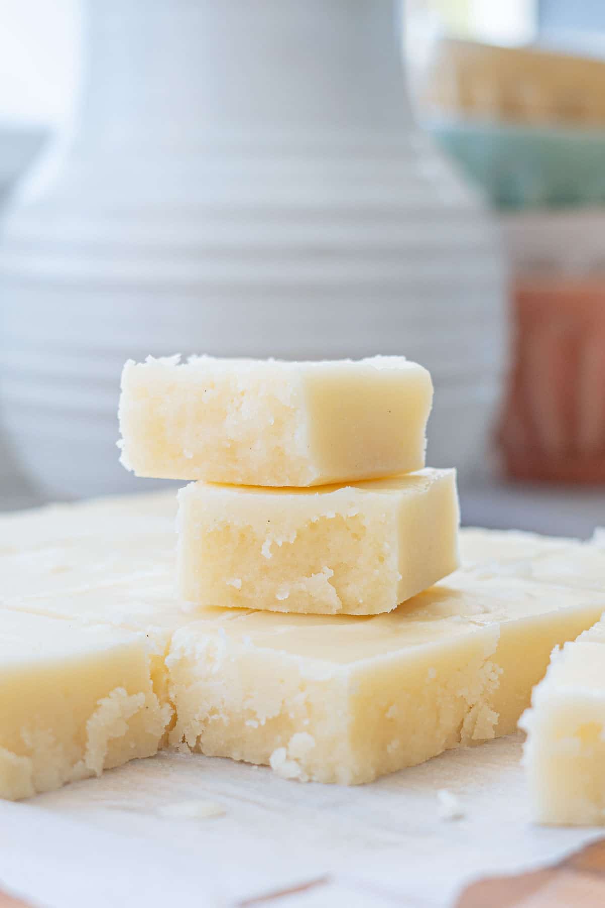 A stack of three pieces of vanilla fudge sitting in front of a white ceramic jug.