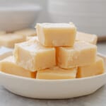 Slices of Vanilla Fudge stacked up on a small white serving dish which is sitting on a bench.