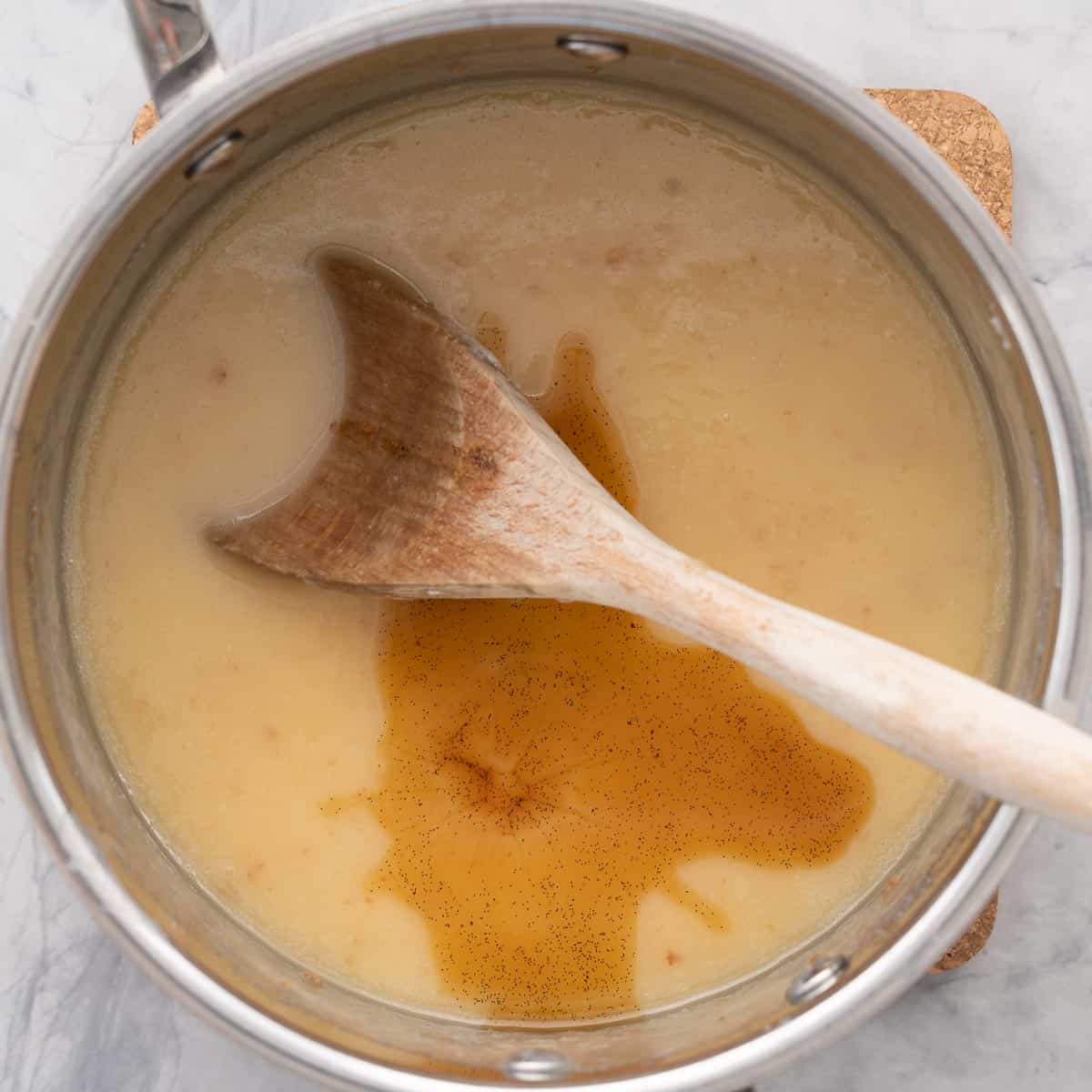 Fudge mixture with vanilla essence added to the saucepan on the bench element with a wooden spoon resting on the side
