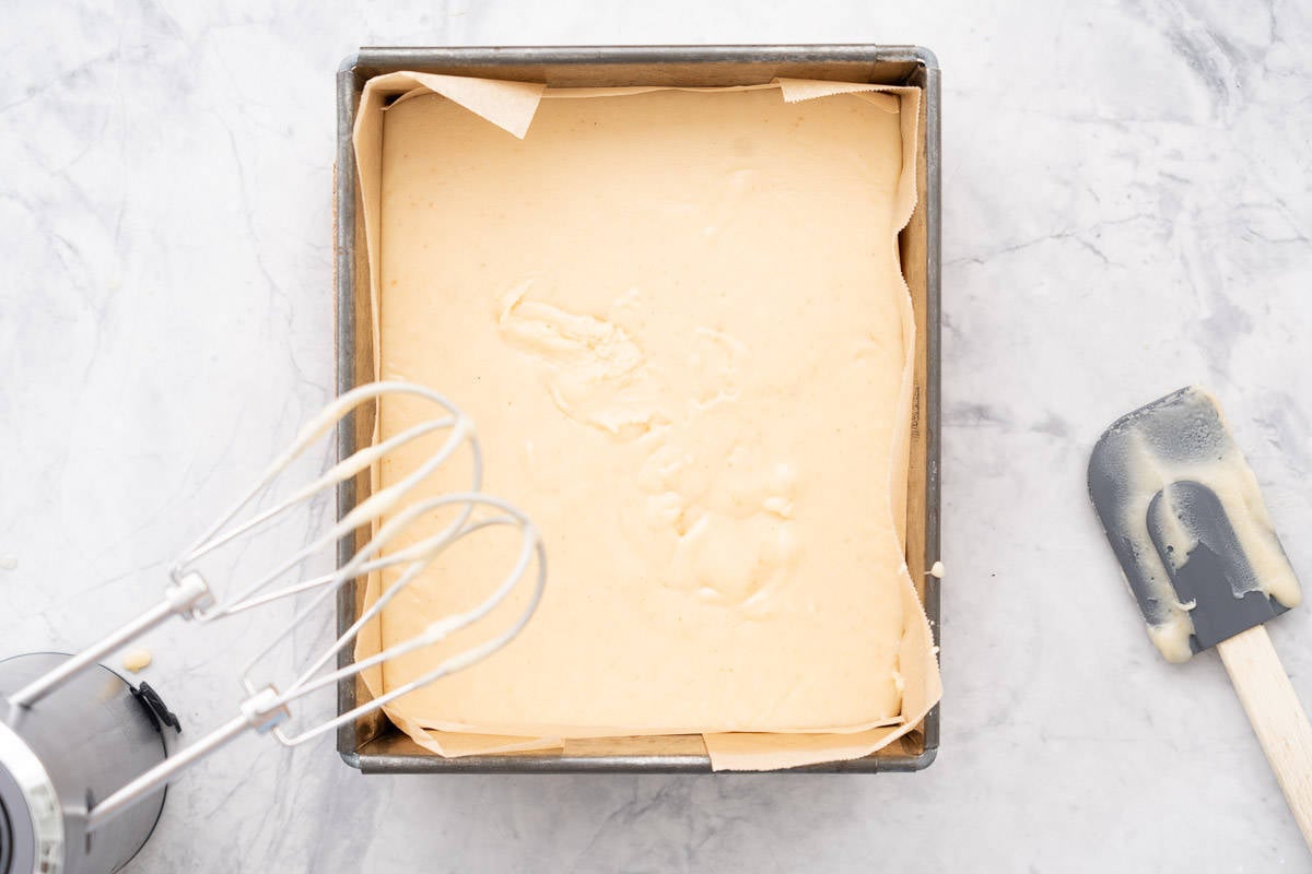 Beaten fudge mixture spread out into a lined baking tin with the beater and spatular sitting to the side.