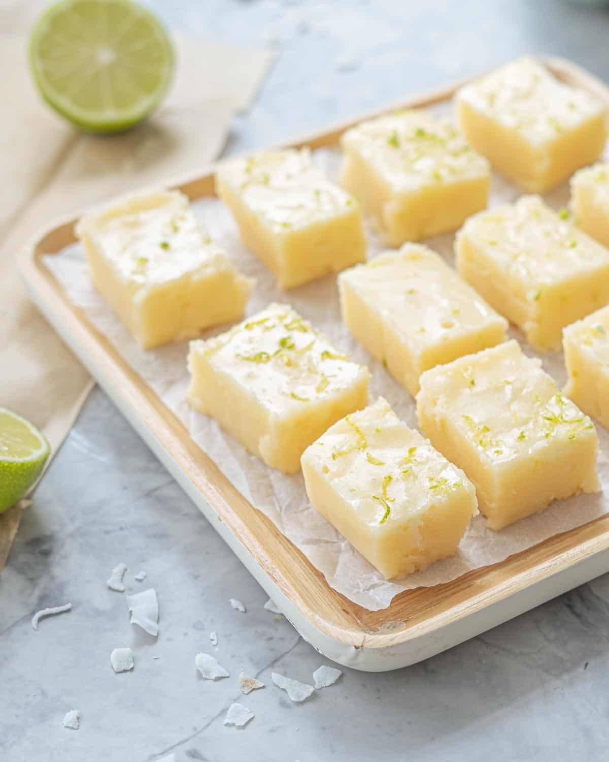 Slices of vegan fudge resting on baking paper and a wooden serving board next to a lime wedge.