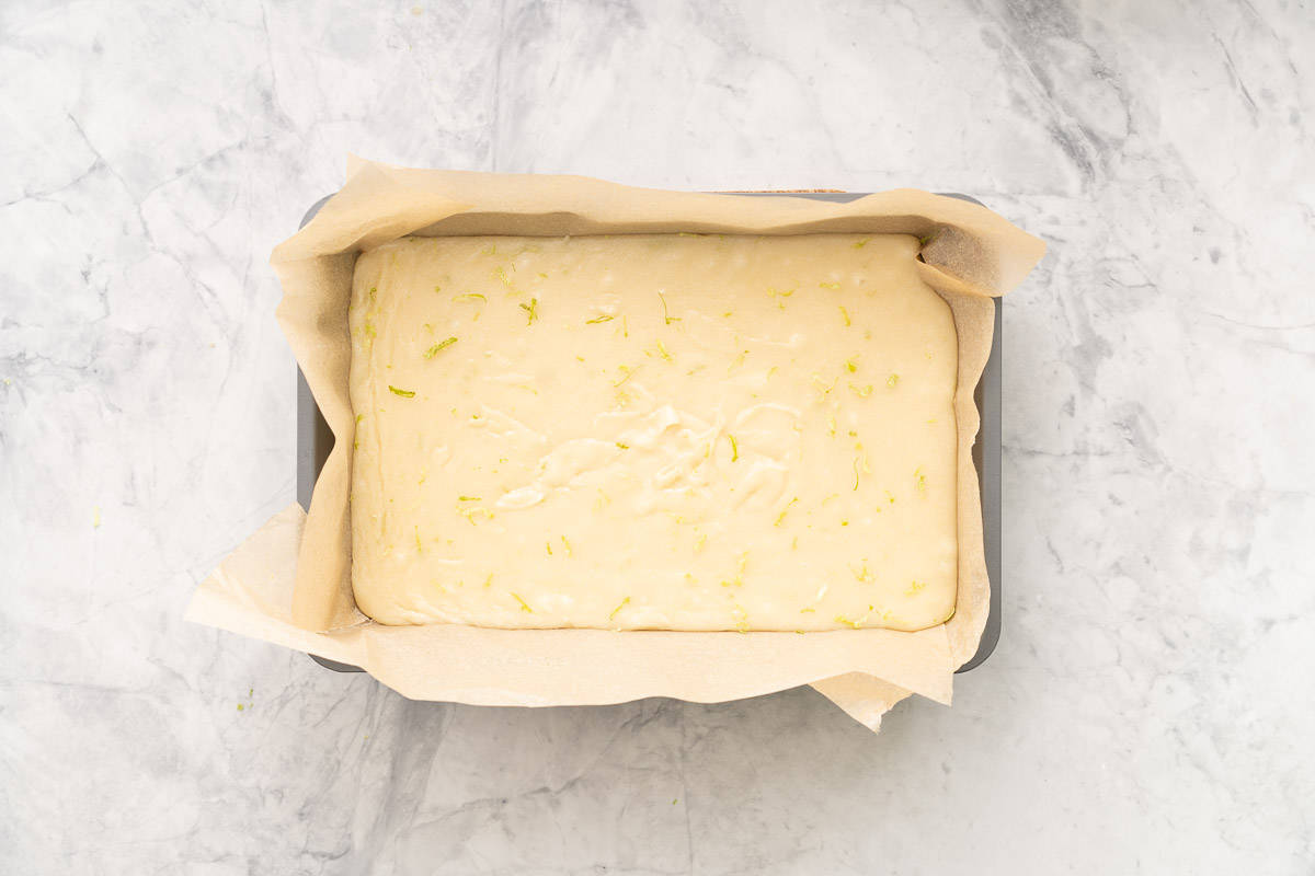A baking tin with brown baking paper and the fudge mixture spread out with a sprinkling of lime zest.