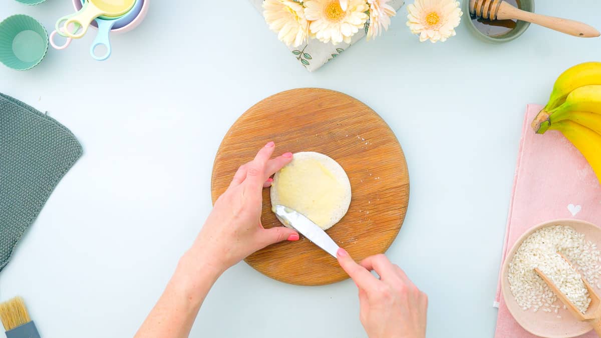 Circle piece of bread with butter being spread onto it.