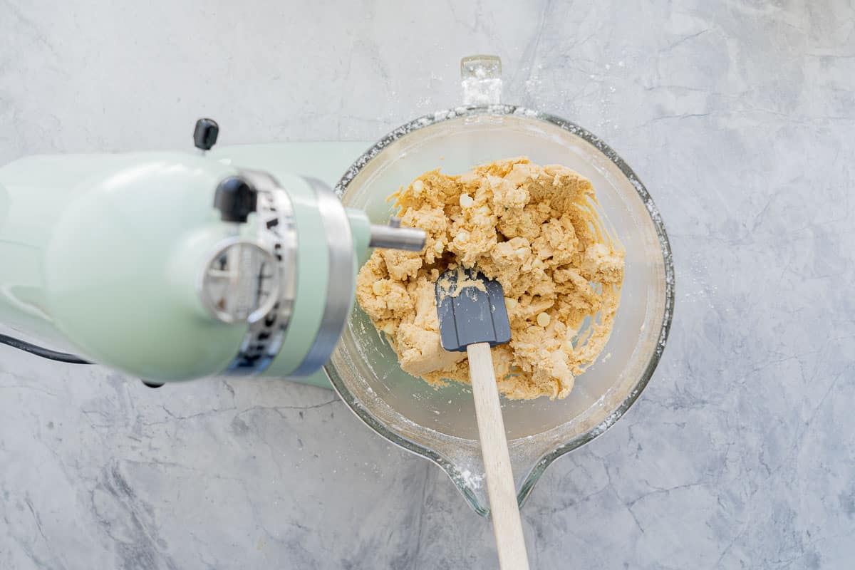 White chocolate chips being folded into the cookie dough mixture with a spatular