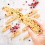 Hand holding a piece of Christmas Biscotti above others on benchtop.