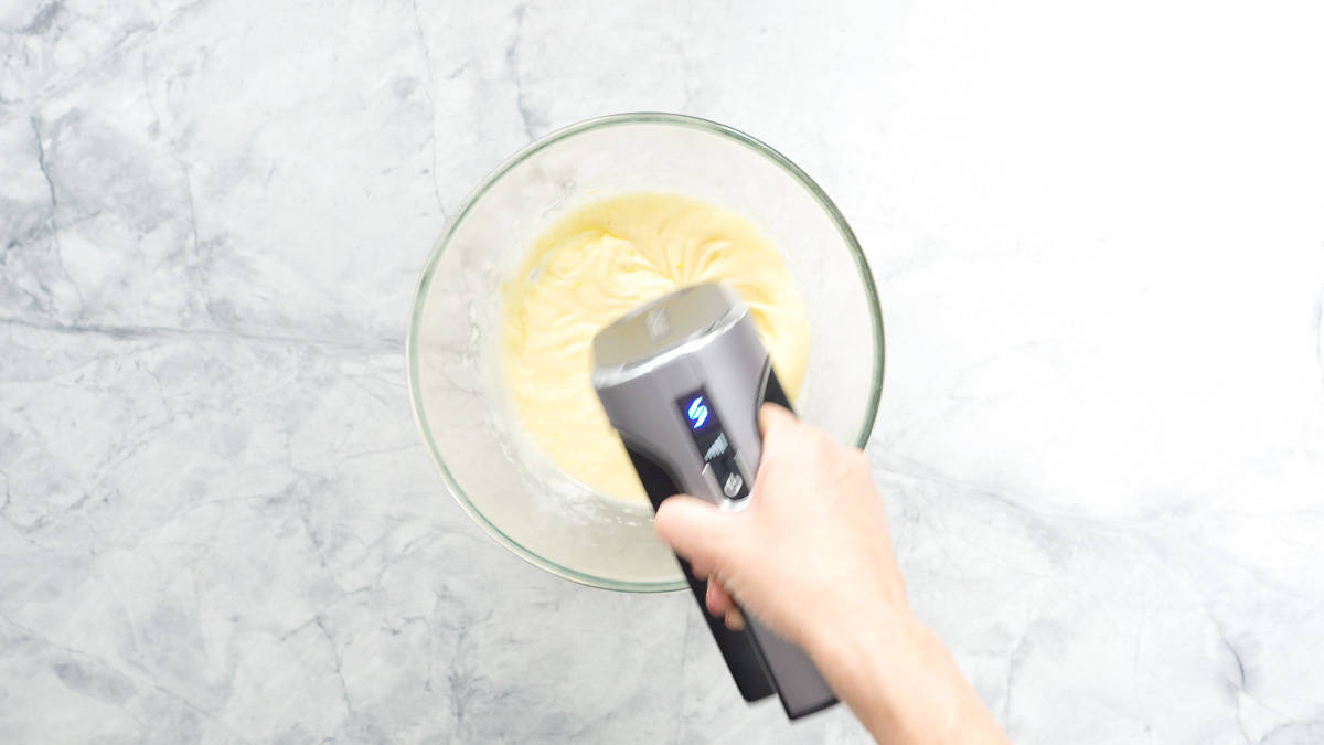 Egg and sugar mixture being beaten with a hand held electric mixer.