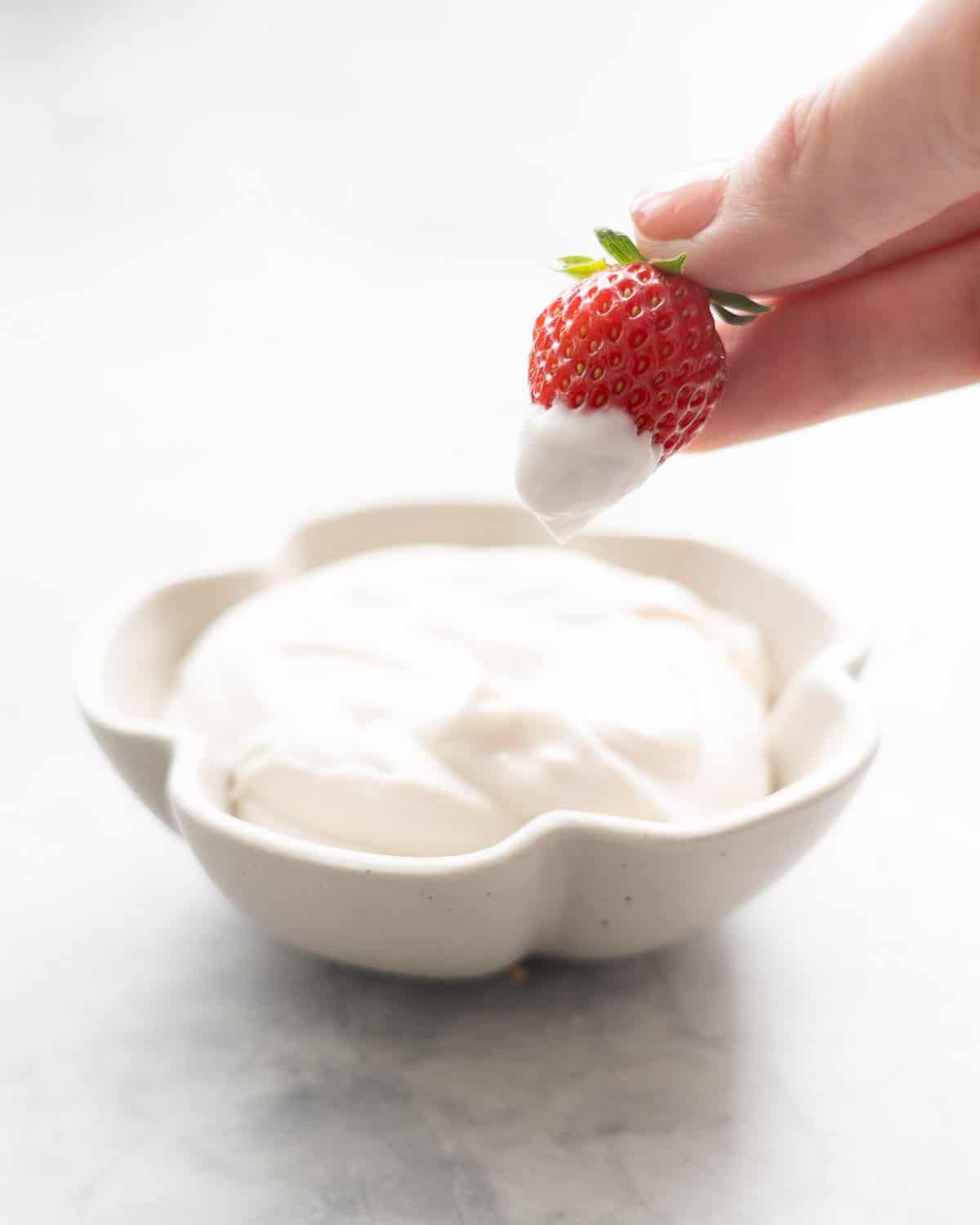 A strawberry being dipped into a small flower shaped bowl of whipped coconut cream