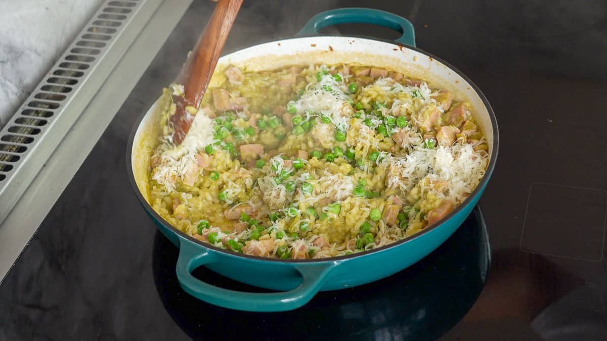 Parmesan cheese being stirred through a pan of pea and ham risotto