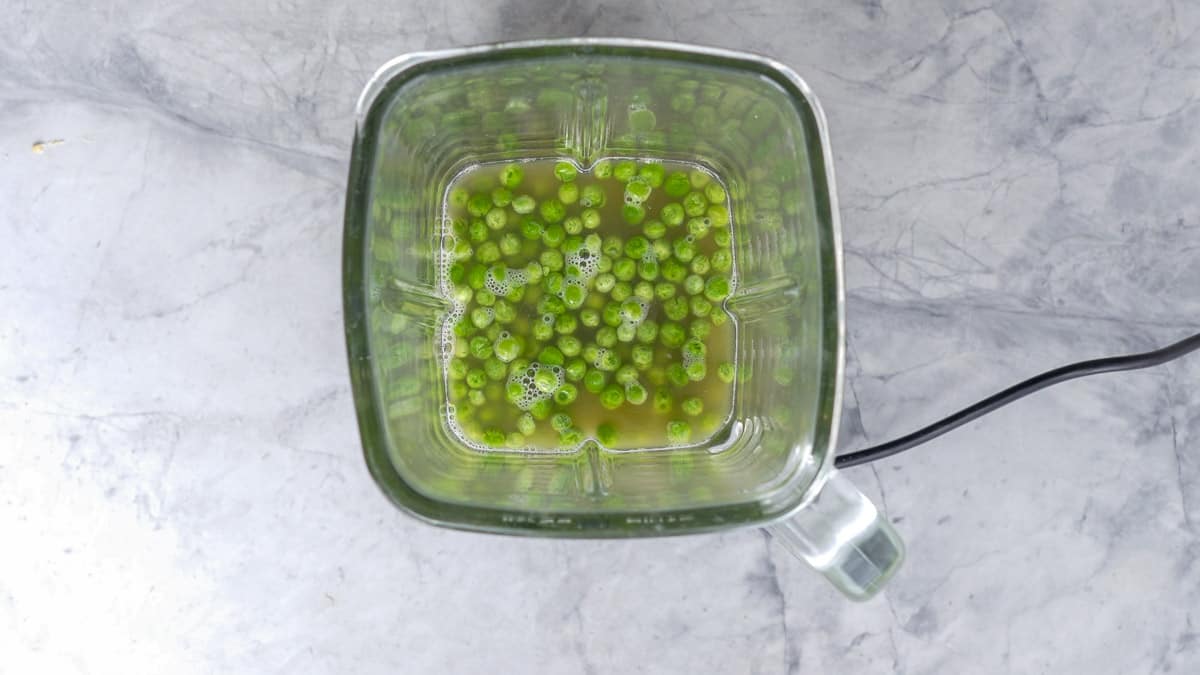 Peas floating in stock in the glass jug of a blender.