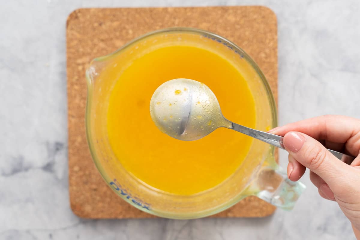 Thickened lemon butter in a glass jug with a spoon held above, coated in the mixture