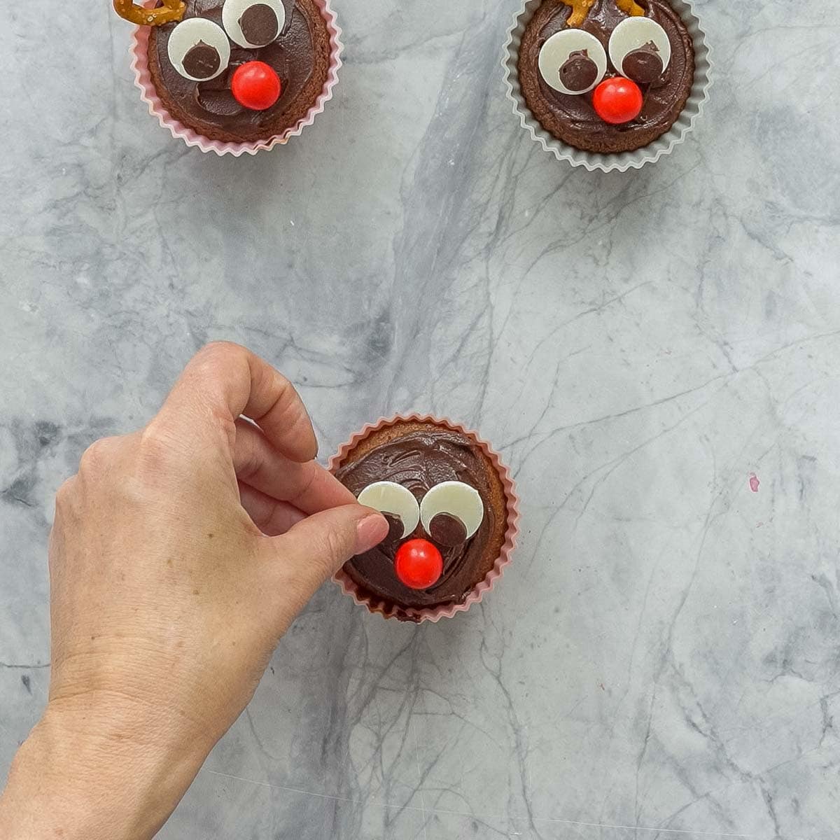 A chocolate frosted cupcake decorated with candy and chocolate buttons to look like eyes and nose.