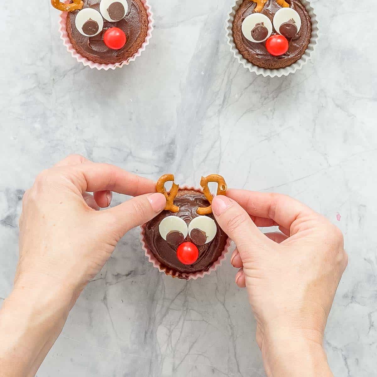 A pretzel snapped in half being placed on a cupcake to look like antlers.