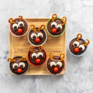 7 reindeer cupcakes on a small wooden tray.