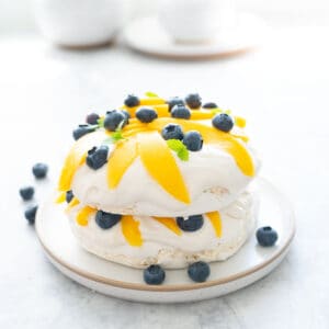 A two layer pavlova topped and filled with whipped cream, sliced mango, blueberries and mint leaves