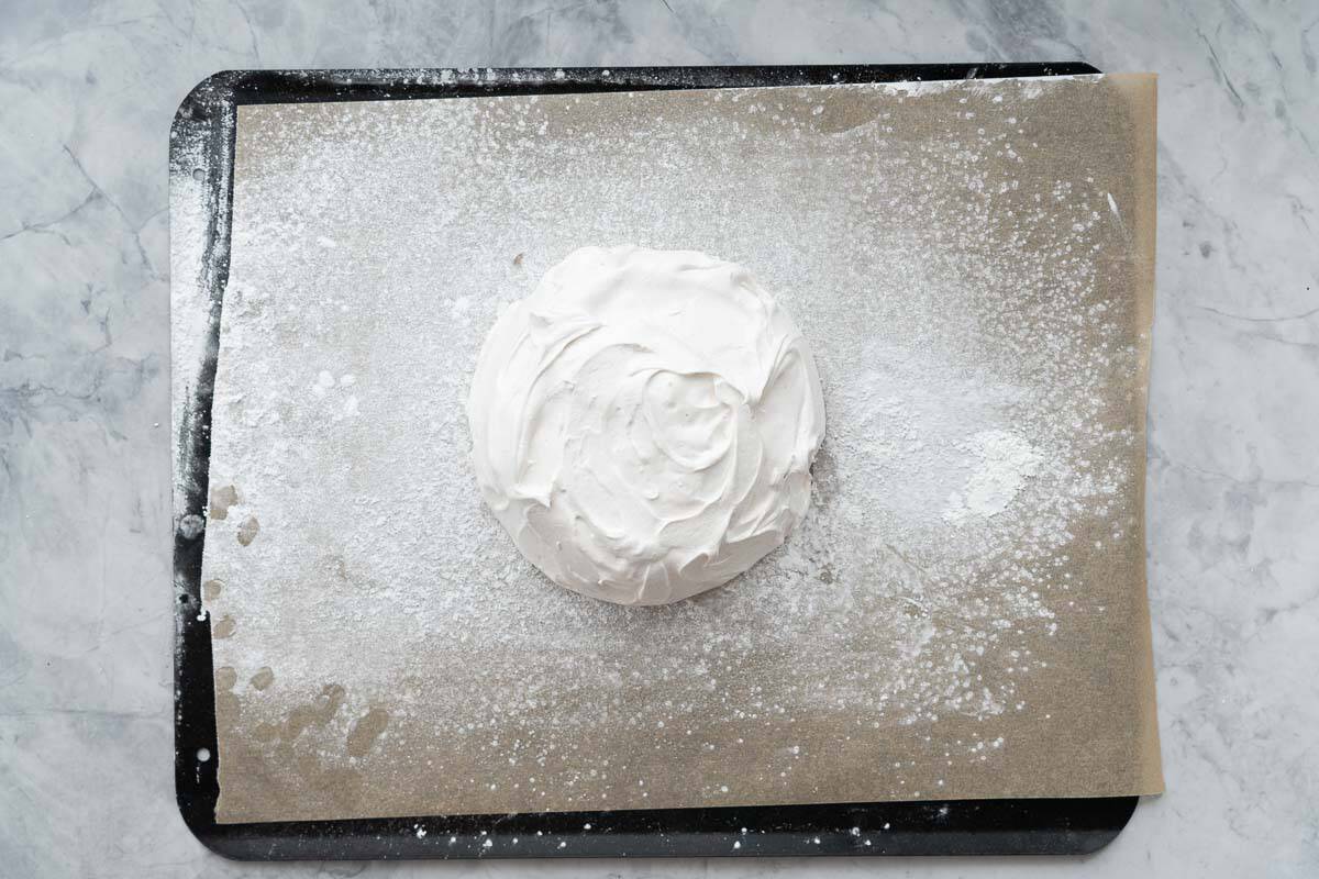 Meringue piled into a circle shape on a lined and dusted baking sheet.